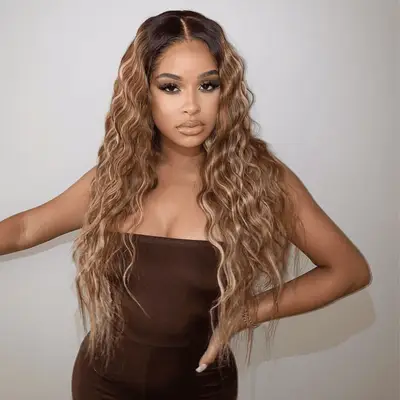 Taina Williams with long, wavy honey blonde hair wearing a strapless outfit posing against a plain backdrop