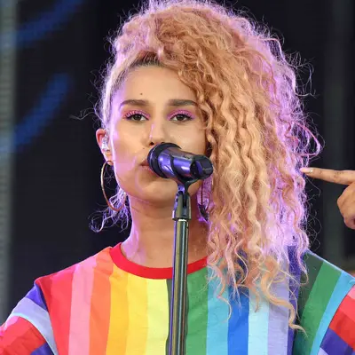 Raye performing with a curly blonde ponytail