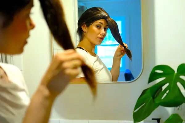 woman brushing out her ponytail in the mirror