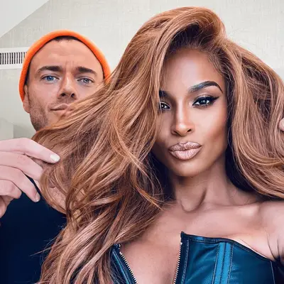 Sarah Rafferty wears her copper hair with copper hue makeup against a wall of roses in a high-neck halter dress 