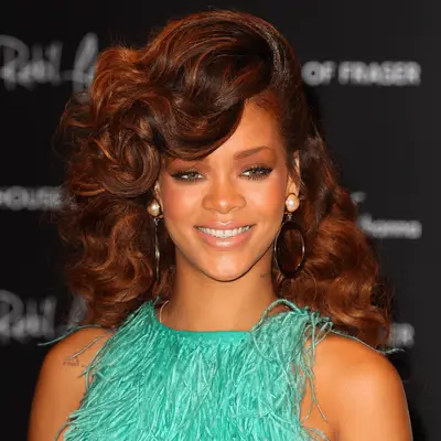 Actress Our Lady J wears her copper hair in an updo with a long face framing side bang, exaggerated cat eye shadow and heavily jeweled earrings