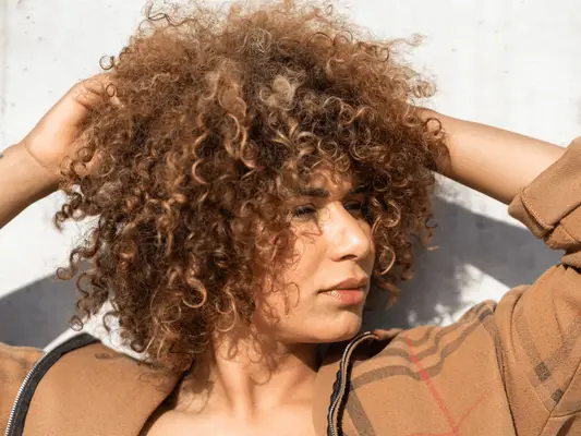 A woman with her hands up, touching her curly hair