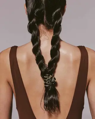 A person with long hair styled in two braids, wearing a dark sleeveless top, shown from the back