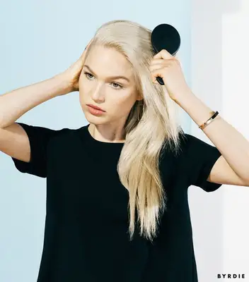 woman brushing her blonde hair back to style into a fishtail braid