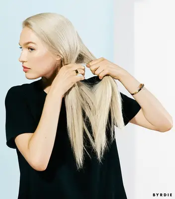 woman parting her blonde hair into two sections to create fishtail braid
