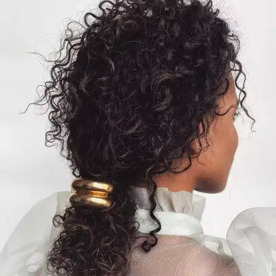 Curly hair pulled back into a ponytail with a gold cuff hair tie