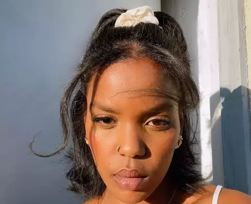 Woman in the sun with a half up half down ponytail and white silk scrunchie