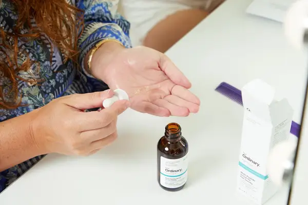 A hand dripping a small amount of The Ordinary Multi-Peptide Serum for Hair Density into the palm of the other hand