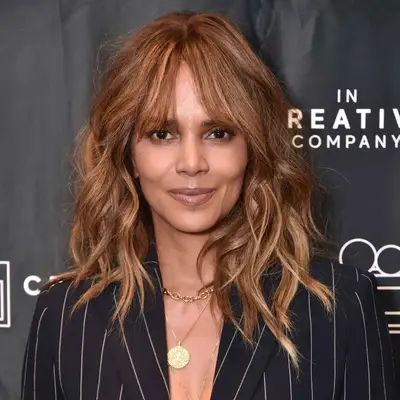 Halle Berry wears a medium-length layered wavy hairstyle with bottleneck bangs