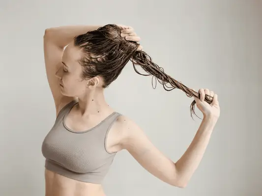 A woman in a sports bra holding her wet hair and pulling at the end