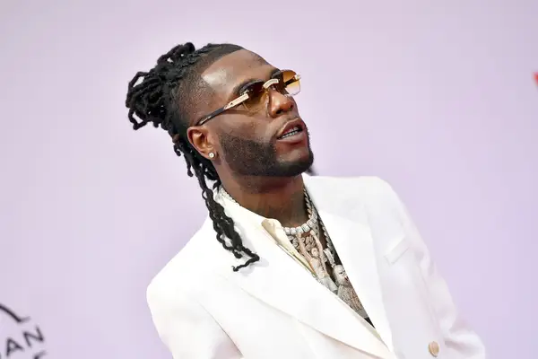 Burna Boy wearing sunglasses a white suit and half up locs in a man bun with half down at the 2021 BET Awards