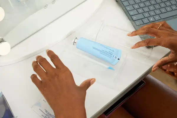 Hands opening Crest Whitening Emulsions Leave-on Teeth Whitening Gel Kit on table near laptop