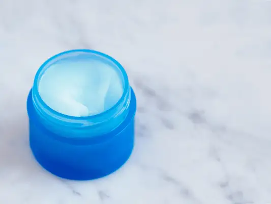 A blue jar with ointment in it, sitting on a marble base