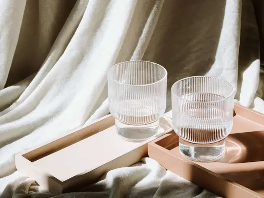 Two glasses of water on trays with textured fabric in the background