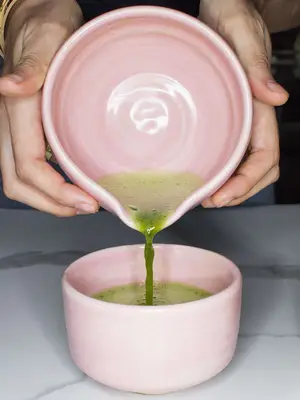 hands pouring green tea into a pink mug