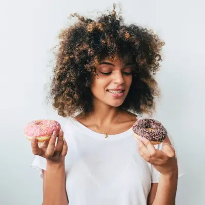 Woman with curly hair looking at two donuts