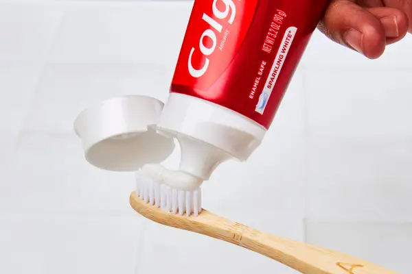 a person squeezing Colgate optic white toothpaste onto a toothbrush