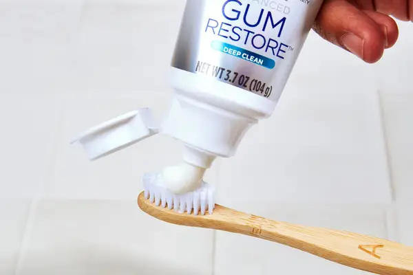 a hand squeezing crest gum restore whitening toothpaste on a toothbrush