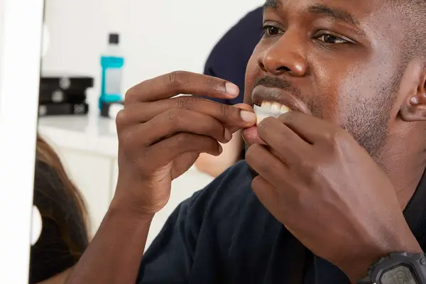 Hands applying Zimba Teeth Whitening Strips to bottom teeth 
