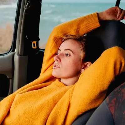 Woman in orange sweater reclining in car seat