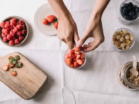 Close up of hands cutting strawberries, blueberries, bananas and oats