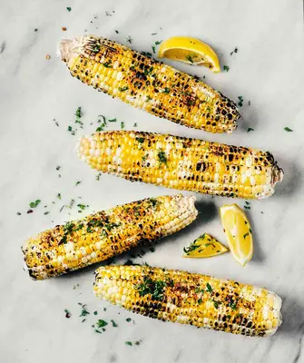 Four corncobs with herb and lemon garnishes 