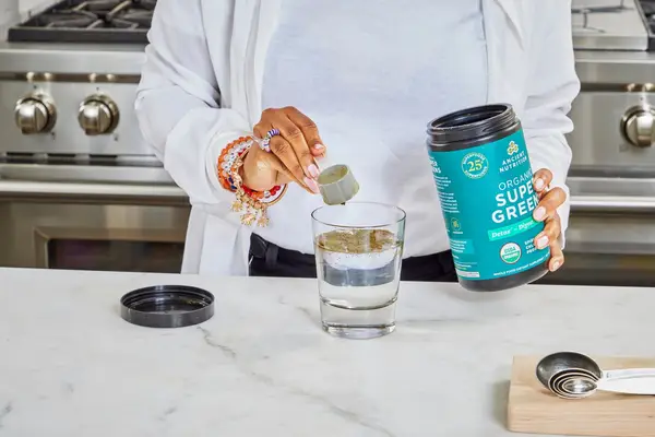 Person scooping Ancient Nutrition Organic SuperGreens into a glass of water