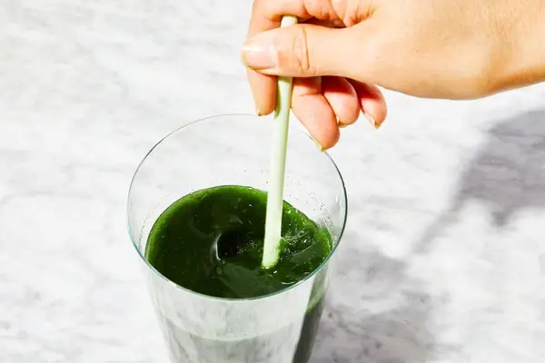 Close-up of hand stirring BioSteel Powdered Greens Antioxidant Superfood in a glass