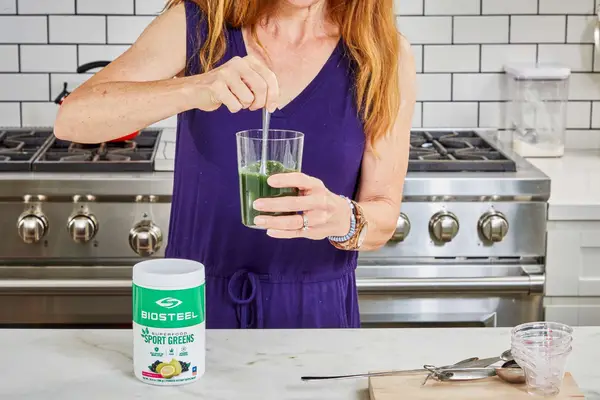 Woman stirs BioSteel Powdered Greens Antioxidant Superfood in a glass of water