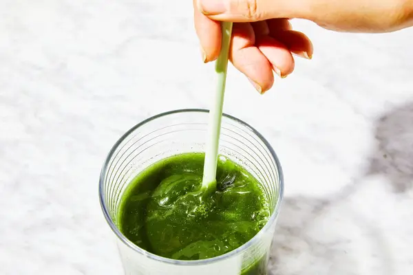 Person stirring a drink using the Ora Organic Easy Being Green Superfood Greens Powder