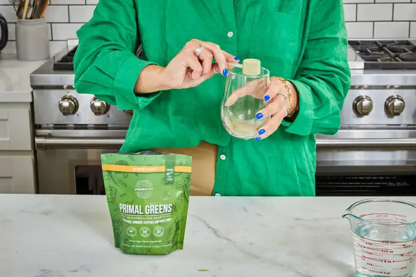 Woman pours Primal Harvest Primal Greens into a glass