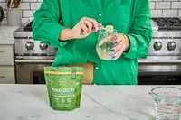 Woman pours Primal Harvest Primal Greens into a glass