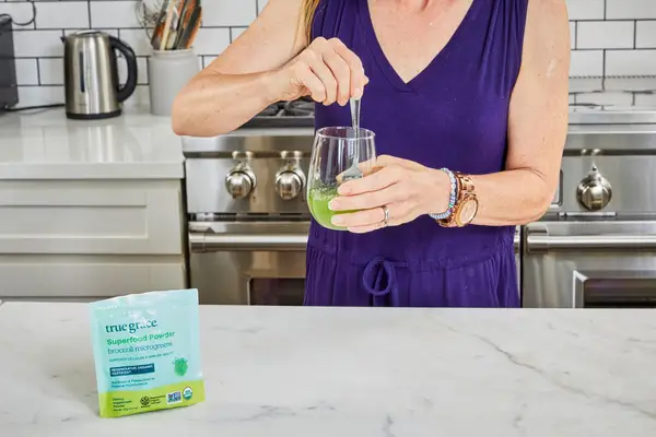 Woman stirs True Grace Superfood Powder Broccoli Microgreens into a glass of water