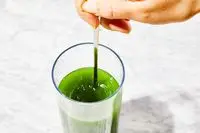 Close-up of hand stirring True Grace Superfood Powder Broccoli Microgreens into a glass of water
