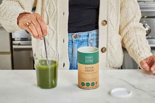 Person stirs Your Super Super Green Mix into a glass of water