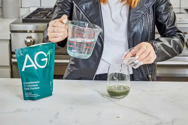 Person pouring water into a glass with AG1 by Athletic Greens