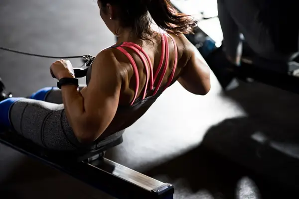 Woman in pink sports bra exercises on a rowing machine.