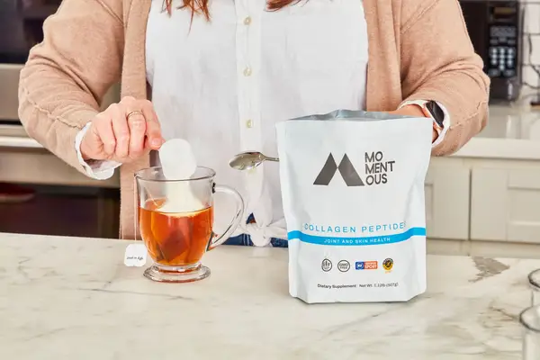 Person pouring a scoop of Momentous Collagen Peptides into a mug of tea