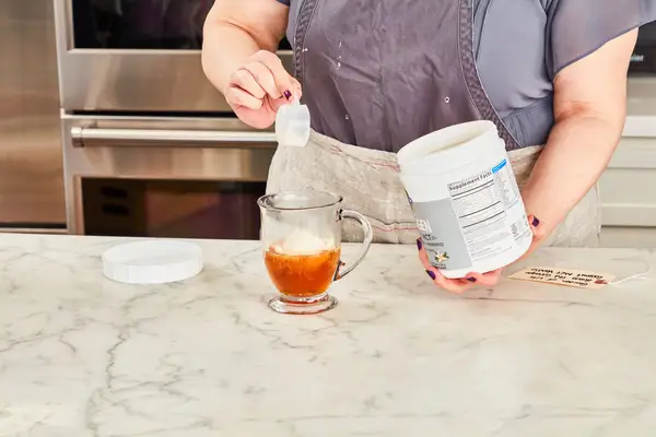 Woman pouring Garden of Life Grass Fed Collagen Coconut MCT Vanilla into a glass of water