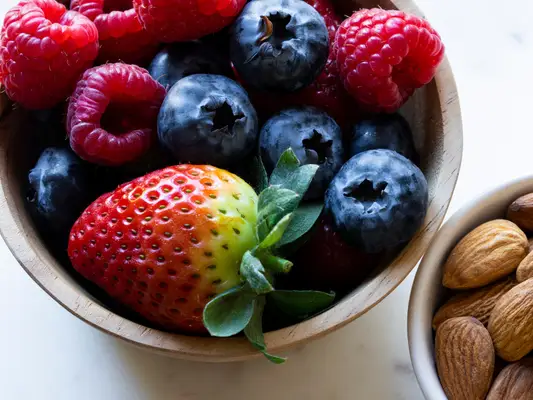 A bowl of raspberries, blueberries and strawberries next to a smaller bowl of almonds