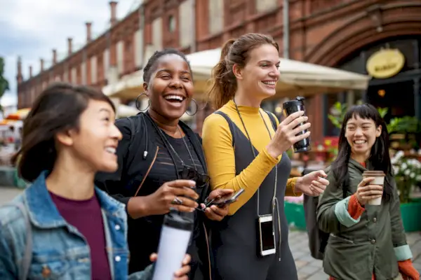 Happy female friends with drinks walking in city