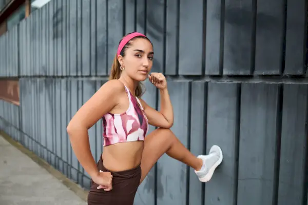 Portrait of a young fit sportswoman looking at the camera while stretching her legs during a cardio workout.