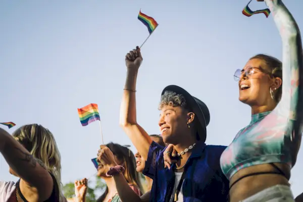 hombre y mujer felices con las manos levantadas sosteniendo banderas del arco iris mientras disfrutan en el desfile del orgullo gay