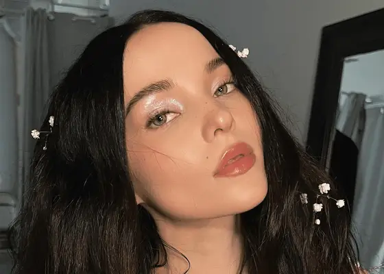 Dove Cameron wears icy glittery eye makeup with little white flowers in her long wavy hair