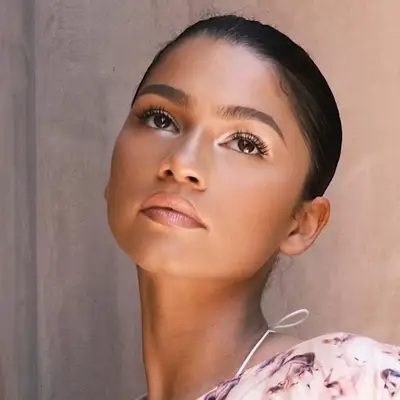 Zendaya wears a radiant makeup with pinkish-nude lipstick, hints of white eyeshadow, and long lashes