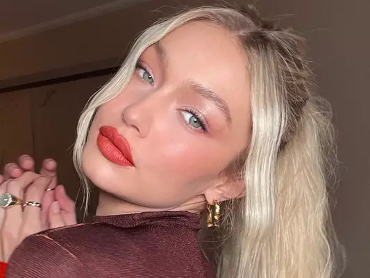 Gigi Hadid wears a radiant, warm-toned makeup look with orange-red lipstick