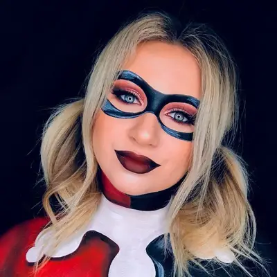 Makeup artist wears Harley Quinn costume featuring pigtails, black eye mask face paint, and burgundy lipstick