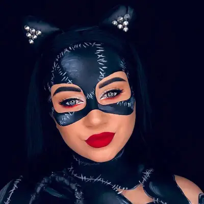 Makeup artist wears Catwoman costume with black eye mask face paint, red lipstick, and multicolored eyeliner