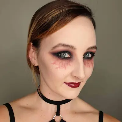Makeup artist wears zombie-inspired dark eyeshadow with veins underneath and red lipstick
