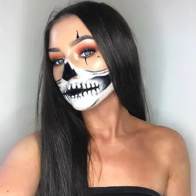 Makeup artist wears half-skull face paint with warm eyeshadow